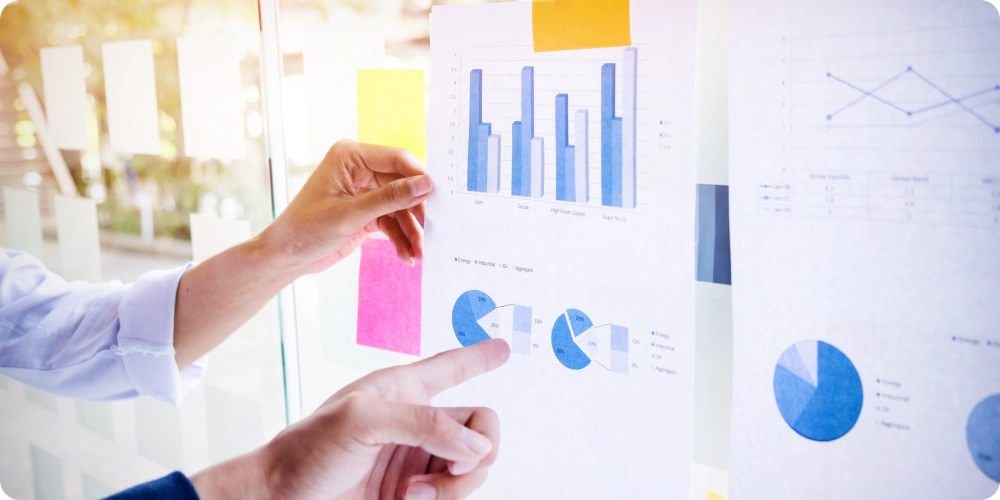 Two people analyzing shipping cost charts and graphs on a glass wall, discussing data-driven decisions.