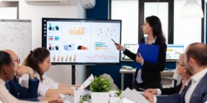 Person presenting stages of custom BI development on a large screen, team members taking notes and discussing the process.