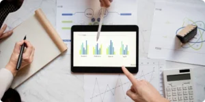 Three people analyzing sales and finance data on a tablet and documents, discussing profitability using BI dashboards.